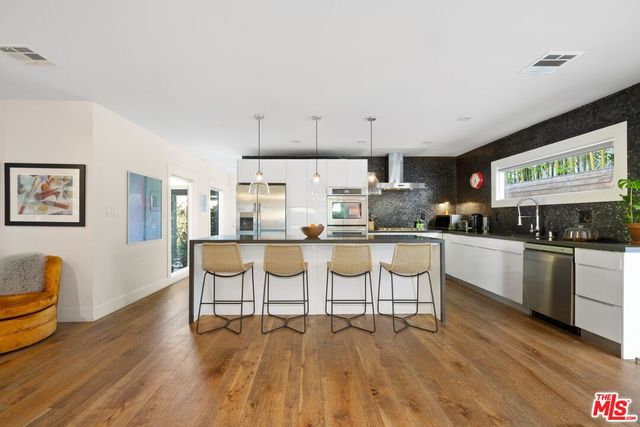 a kitchen with stainless steel appliances kitchen island granite countertop a stove a sink and white cabinets with wooden floor