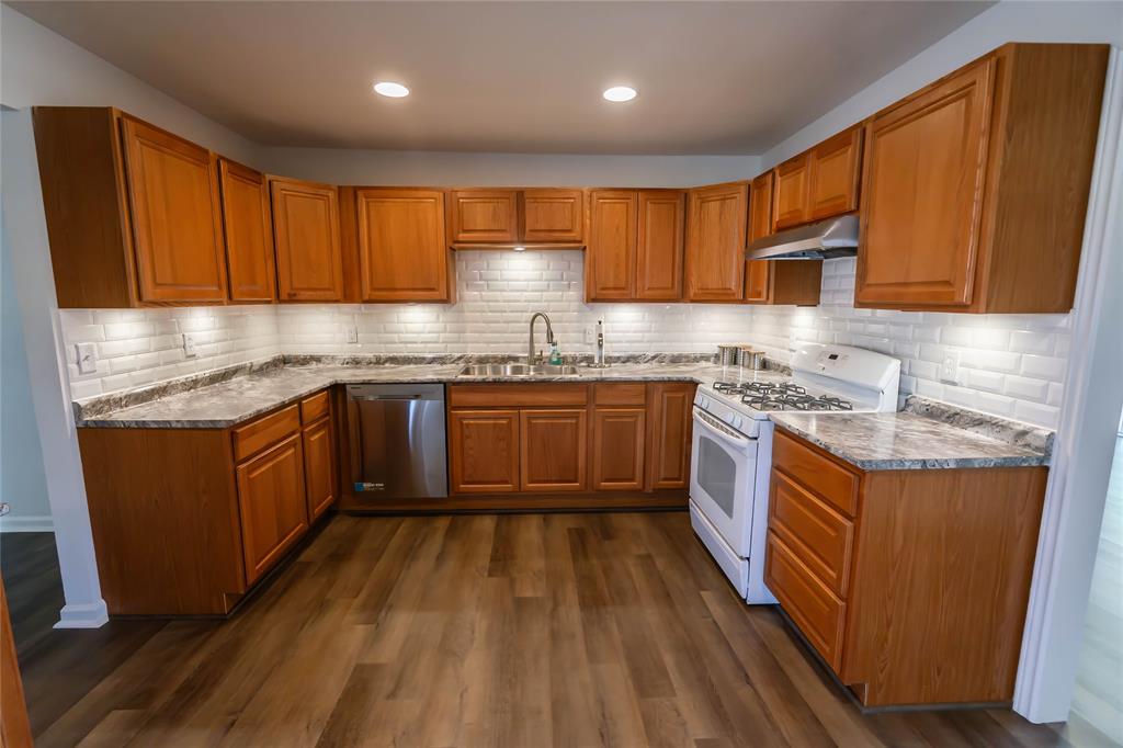 1226 Clay Street Nocona, TX 76255 - Photo 12 of 31 a kitchen with stainless steel appliances granite countertop wooden cabinets a sink dishwasher a stove and a refrigerator with wooden floor