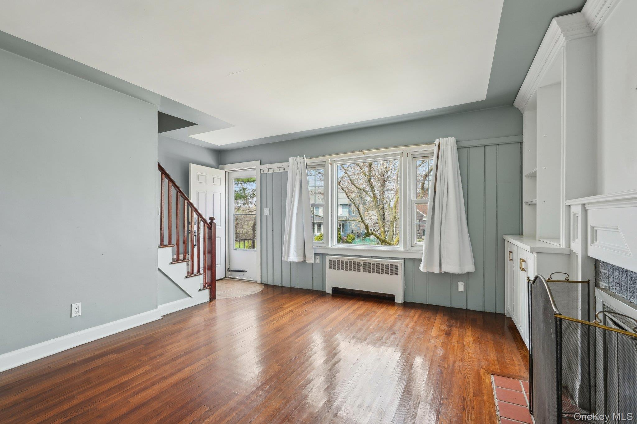 12 Highview Avenue Rye Brook, NY 10573 - Photo 7 of 19 Unfurnished living room with baseboards, a fireplace with flush hearth, wood finished floors, radiator heating unit, and stairs