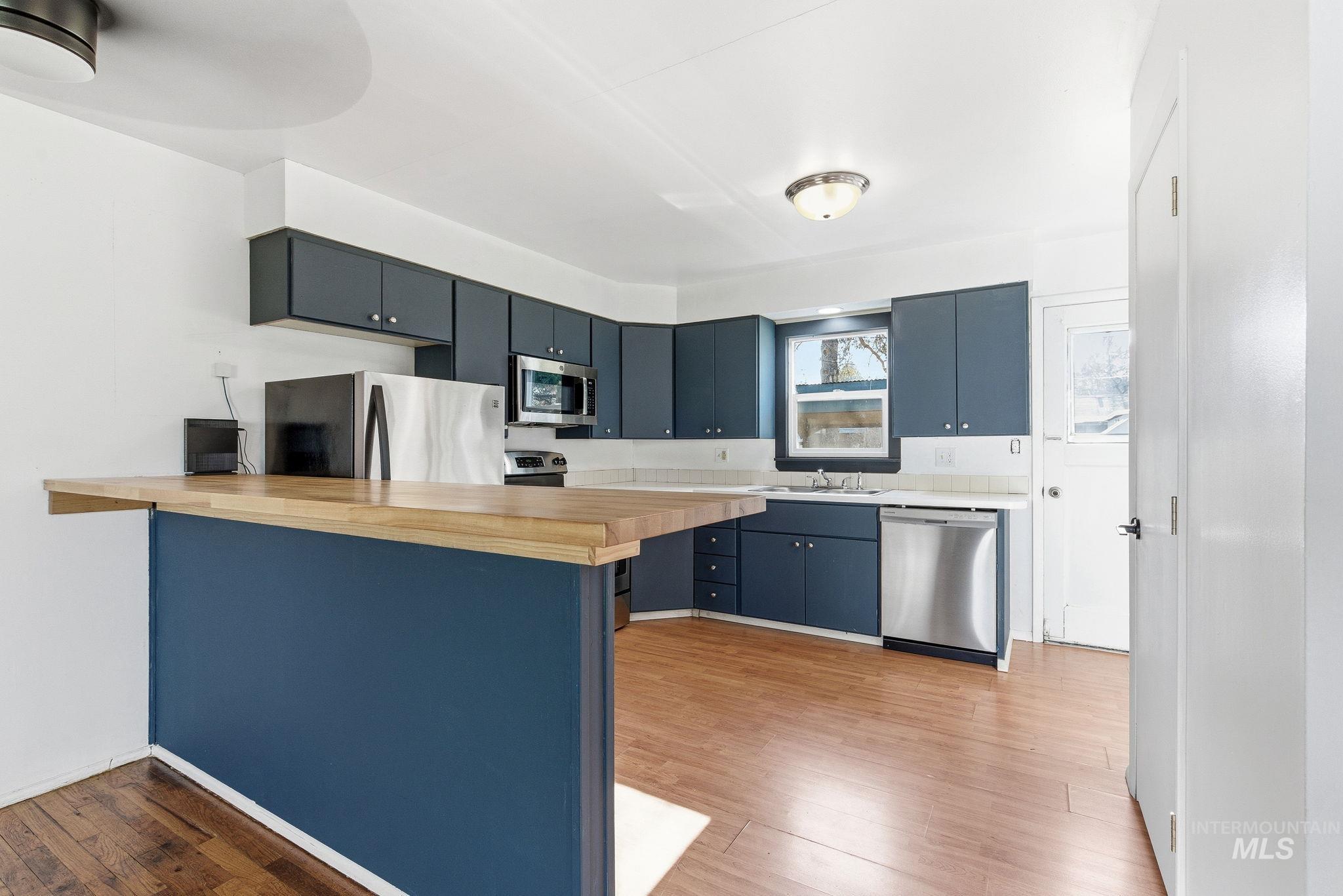 5603 West Edson Street Boise, ID 83705 - Photo 16 of 43 Kitchen with a peninsula, butcher block counters, appliances with stainless steel finishes, blue cabinets, and light wood-style flooring