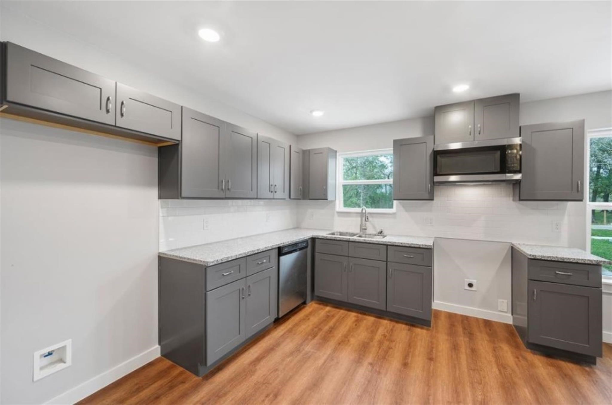 8120 Laura Koppe Road, Unit B Houston, TX 77028 - Photo 7 of 25 This modern kitchen features sleek gray cabinets, stainless steel appliances, and granite countertops. It has ample natural light from large windows and a stylish, open layout with wood-look flooring.