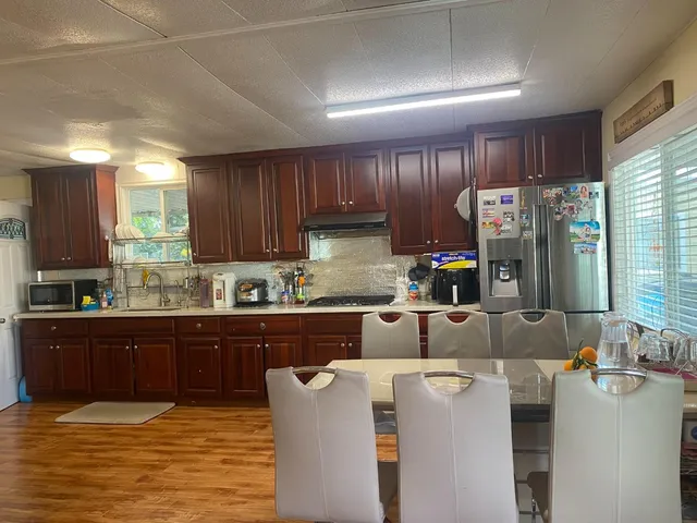 a kitchen with stainless steel appliances granite countertop a sink dishwasher a refrigerator a stove with wooden cabinets and floor