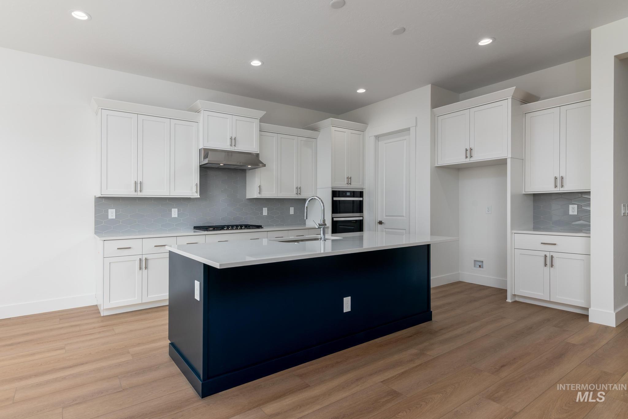 5403 Juliet Rose Avenue Caldwell, ID 83607 - Photo 5 of 12 Modern kitchen featuring a contrasting navy island with a light-toned countertop, white cabinetry with silver hardware, integrated stainless steel appliances, and wood-finish flooring