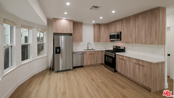 a kitchen with stainless steel appliances granite countertop a refrigerator a sink dishwasher a stove and a microwave oven with wooden floor