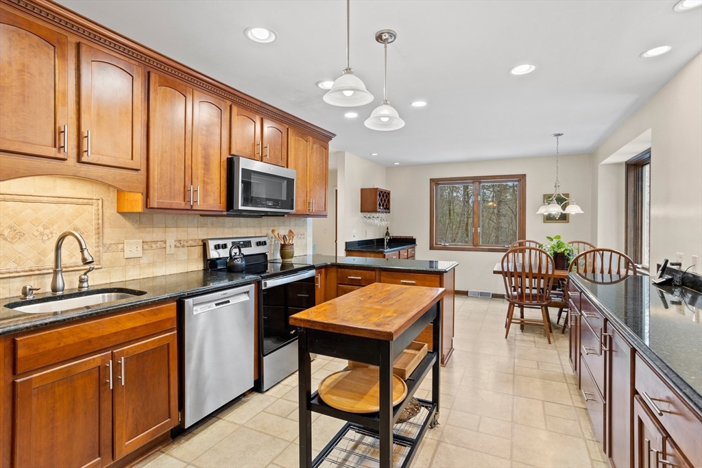 88 Coventry Wood Road Bolton, MA 01740 - Photo 11 of 41 a kitchen with stainless steel appliances granite countertop a stove top oven a sink dishwasher a dining table and chairs with wooden cabinets