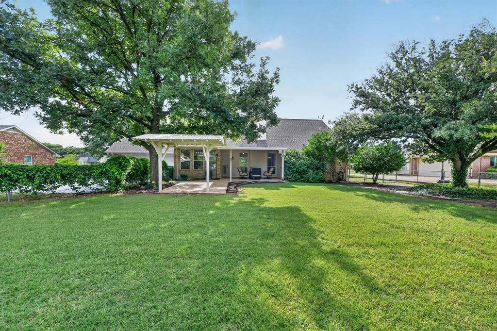 421 Ben Boyd Road Argyle, TX 76226 - Photo 19 of 25 Expansive lawn with mature trees and a privacy hedge, featuring a covered patio with a white pergola structure and a concrete slab