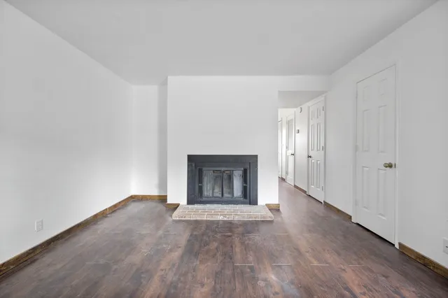 a view of an empty room with wooden floor fireplace and a window