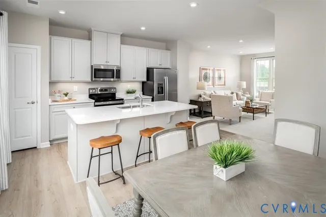 a kitchen with stainless steel appliances kitchen island granite countertop a refrigerator a stove a sink a dining table and chairs with wooden floor