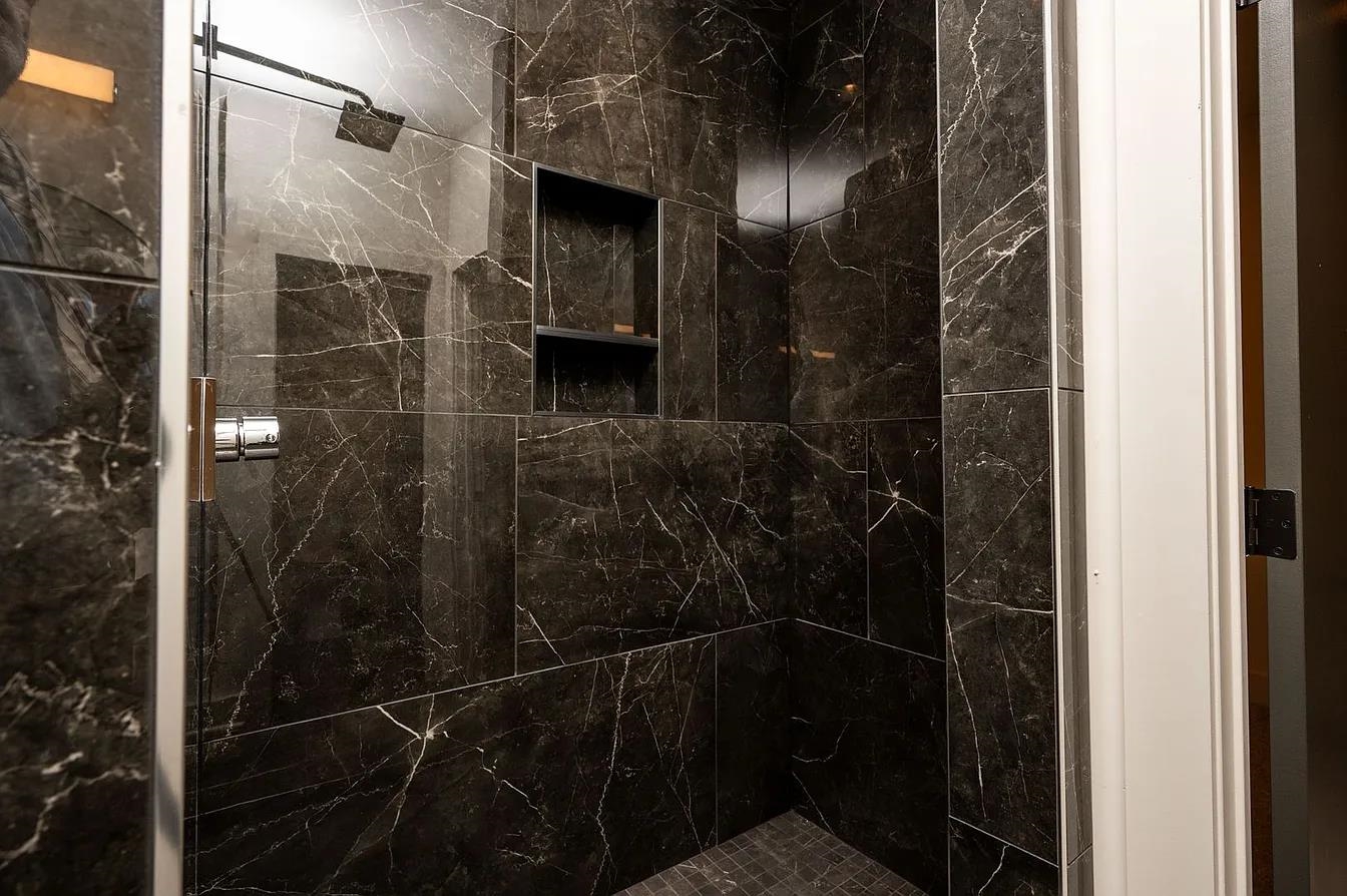 752 Meda Street Memphis, TN 38104 - Photo 7 of 18 Shower enclosure featuring dark marbled tile, clear glass door, built-in shower niche, and a rain showerhead