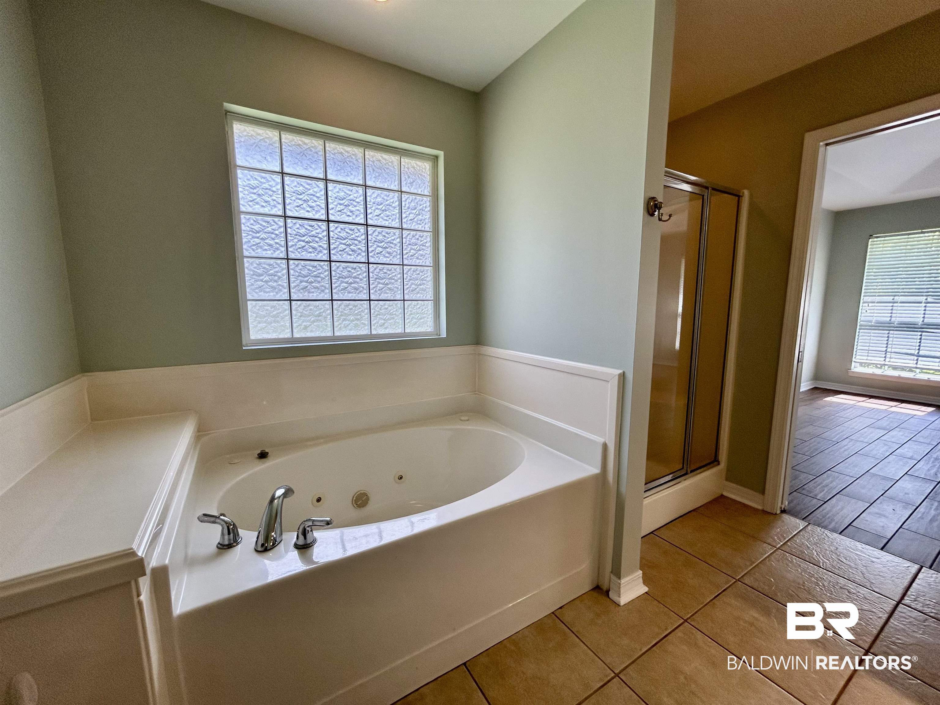 7198 Raintree Lane Gulf Shores, AL 36542 - Photo 18 of 33 Spacious bathroom featuring a jetted soaking tub with chrome fixtures, a glass block window, tile flooring, and a glass-enclosed shower