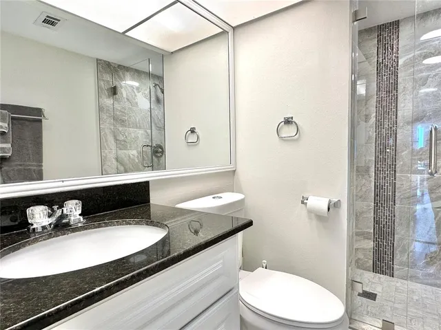 a bathroom with a granite countertop sink a toilet a mirror and shower