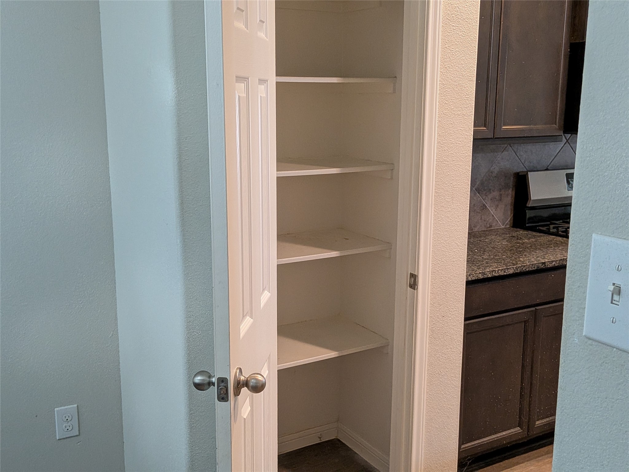 15730 Joe Dimaggio Street Splendora, TX 77372 - Photo 11 of 20 This photo shows a small pantry with several white shelves, ideal for extra storage. Adjacent is part of a kitchen with dark cabinetry and granite countertops.
