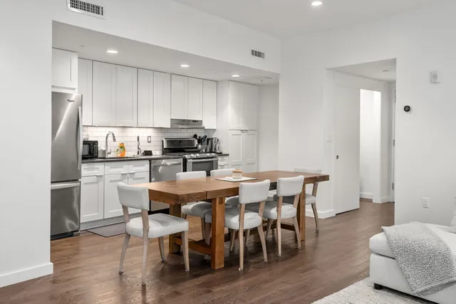 a kitchen with stainless steel appliances granite countertop a dining table chairs refrigerator and sink