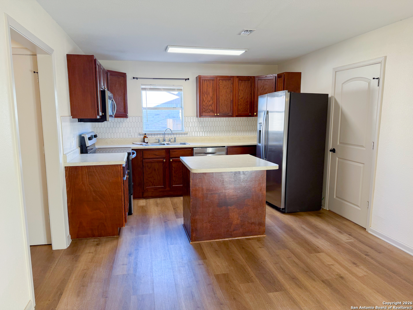 409 Coughran Street Pleasanton, TX 78064 - Photo 2 of 16 a kitchen with stainless steel appliances a refrigerator a sink a stove a microwave and wooden floors