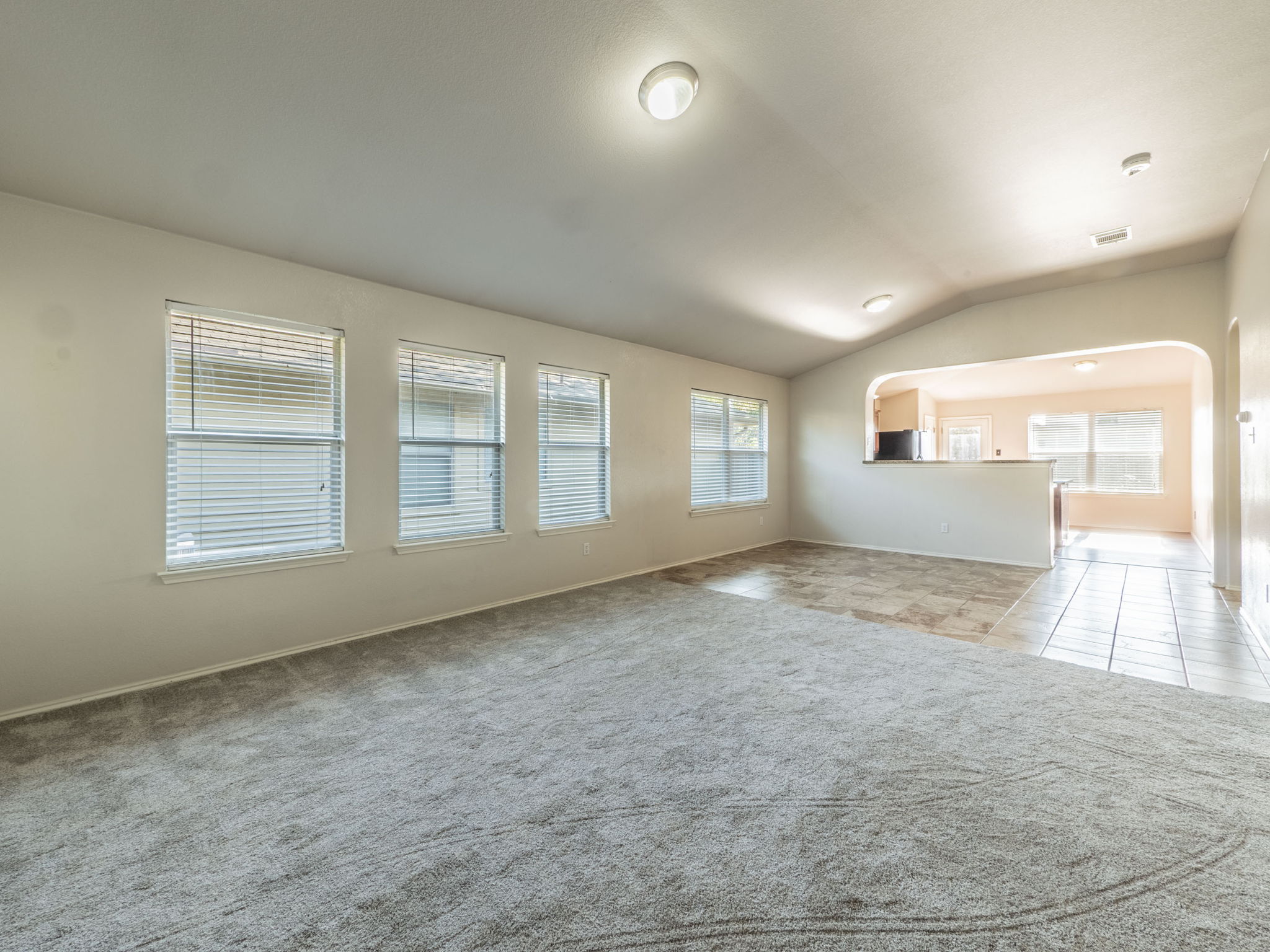 3209 Wickham Lane Austin, TX 78725 - Photo 4 of 26 Unfurnished living room with arched walkways, vaulted ceiling, light carpet, and light tile patterned flooring
