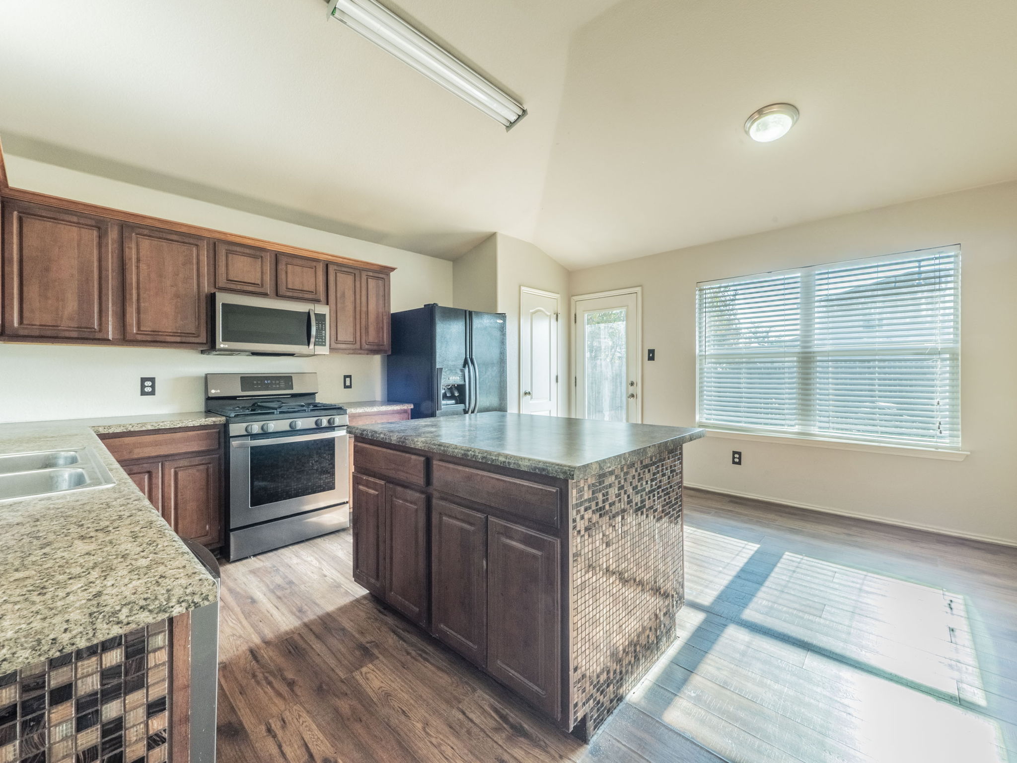 3209 Wickham Lane Austin, TX 78725 - Photo 6 of 26 Kitchen featuring dark brown cabinetry, stainless steel appliances, dark wood-type flooring, a center island, and vaulted ceiling
