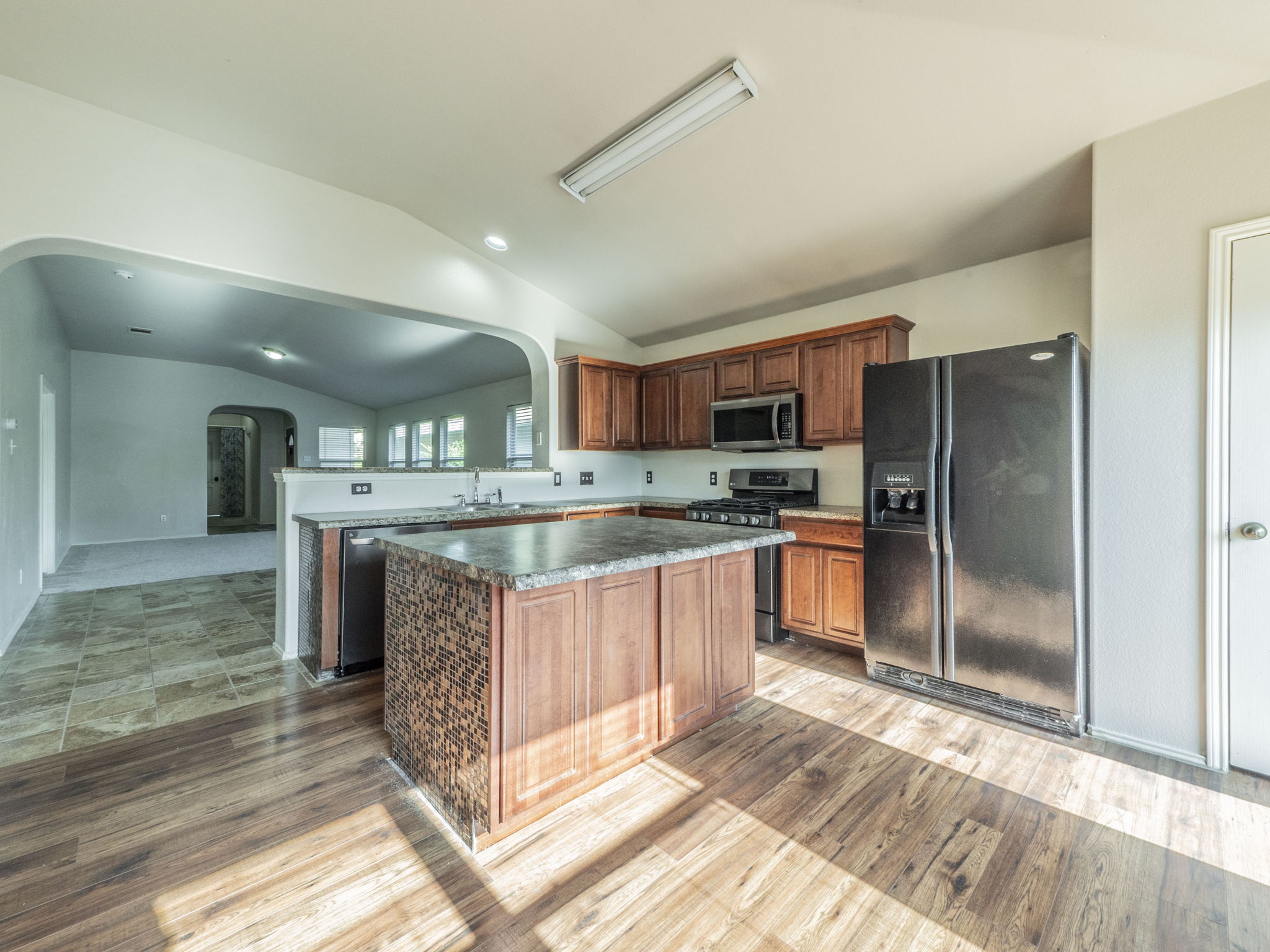 3209 Wickham Lane Austin, TX 78725 - Photo 7 of 26 Kitchen featuring stainless steel appliances, a center island, arched walkways, lofted ceiling, and dark countertops
