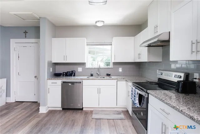 a kitchen with cabinets appliances wooden floor and a window