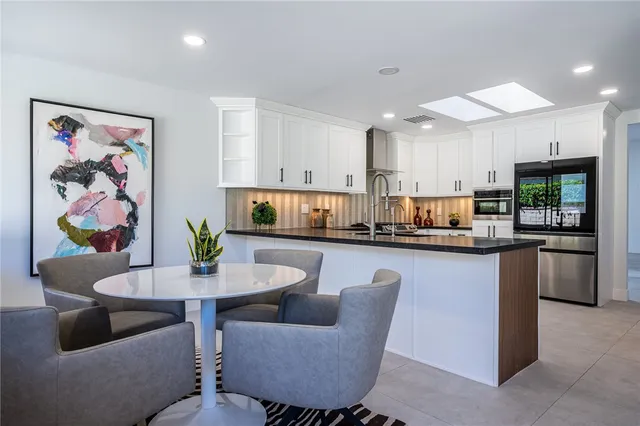 a kitchen with stainless steel appliances kitchen island granite countertop a dining table chairs and a refrigerator