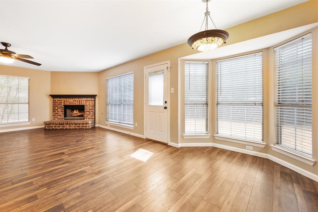 7517 Point Reyes Drive Fort Worth, TX 76137 - Photo 5 of 30 Spacious interior with wood-finish flooring, a brick fireplace with a dark mantel, a ceiling fan, a contemporary chandelier, and a bay window configuration