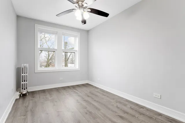 an empty room with wooden floor chandelier fan and windows