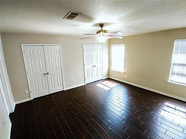 an empty room with wooden floor chandelier fan and windows