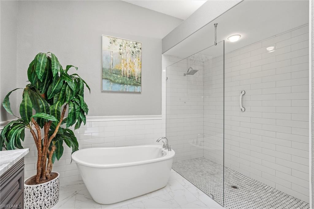 3033 Olde Cove Way Naples, FL 34119 - Photo 29 of 49 Full bath with a shower stall, a freestanding bath, wainscoting, vanity, and tile walls