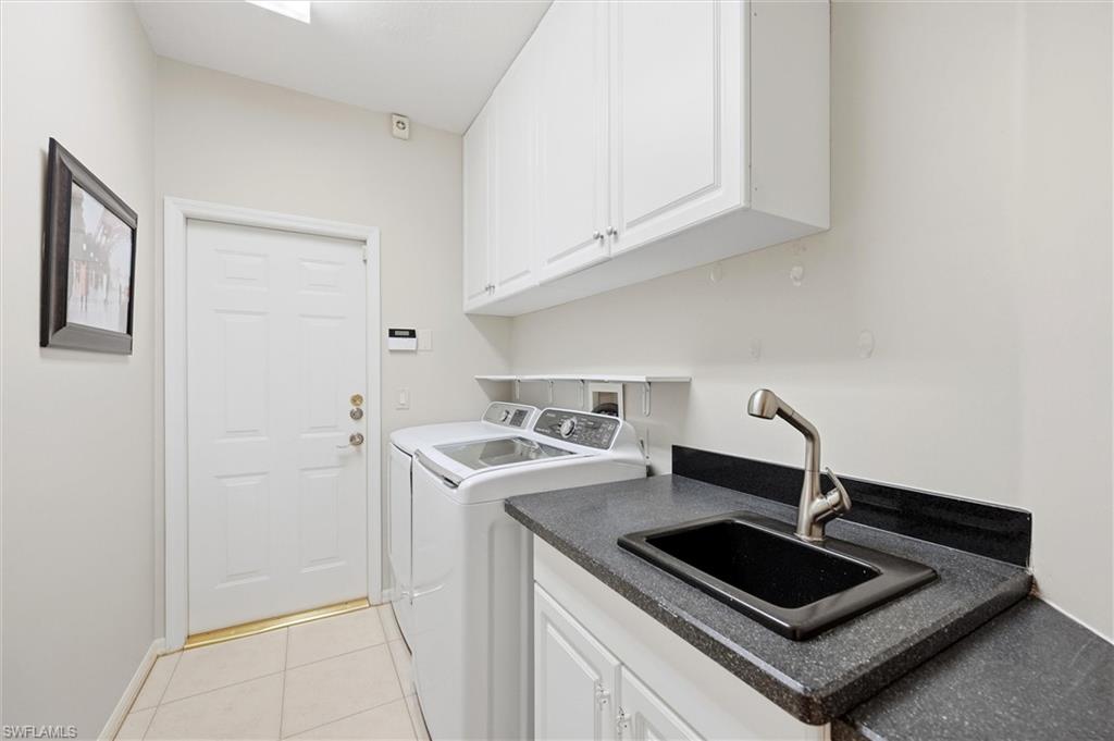 3033 Olde Cove Way Naples, FL 34119 - Photo 42 of 49 Sink with cabinet space, light tile patterned floors, and washing machine and dryer with garage access