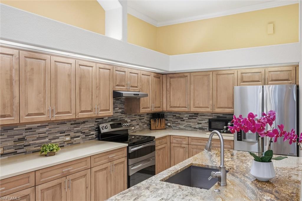 3033 Olde Cove Way Naples, FL 34119 - Photo 10 of 49 Kitchen with appliances with stainless steel finishes, light stone counters, light brown cabinetry, under cabinet range hood, and ornamental molding