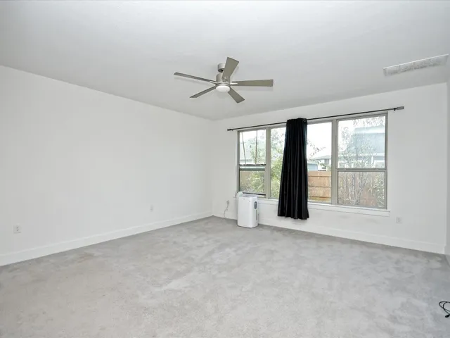 an empty room with chandelier fan and windows