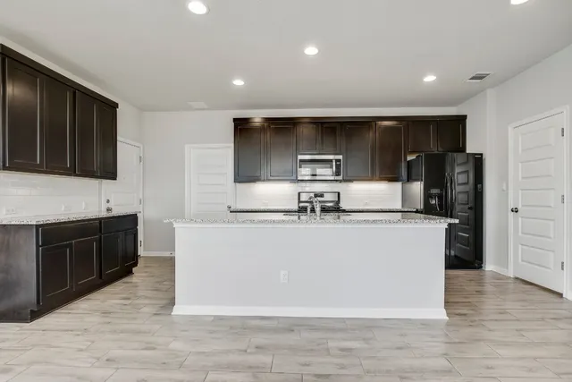 a large kitchen with stainless steel appliances a large counter top a stove a microwave a sink and a refrigerator