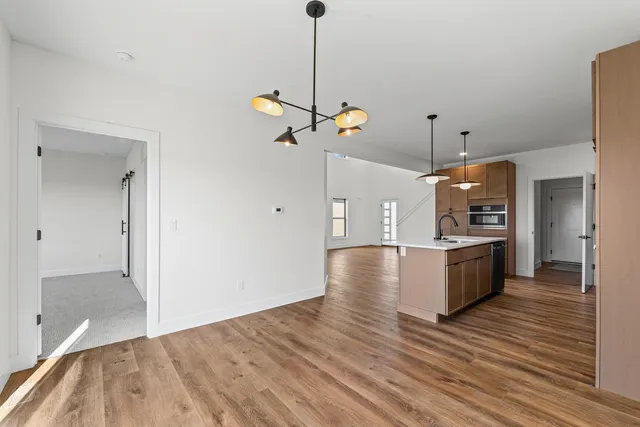 a view of an empty room and kitchen with wooden floor