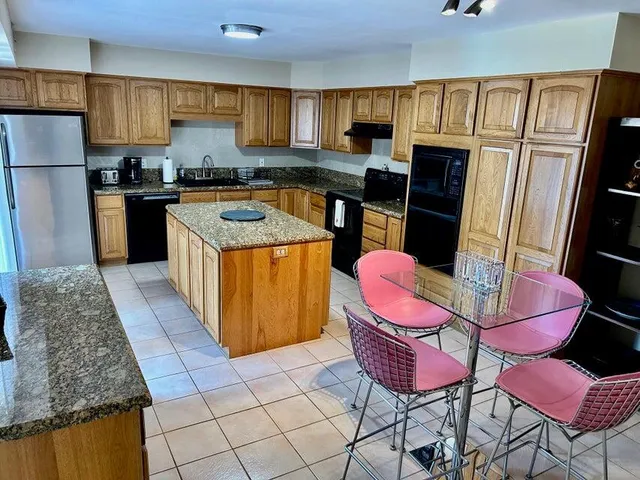 a kitchen with stainless steel appliances kitchen island granite countertop a refrigerator a sink dishwasher a dining table and chairs with wooden floor