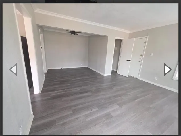 a view of an empty room with wooden floor and a ceiling fan