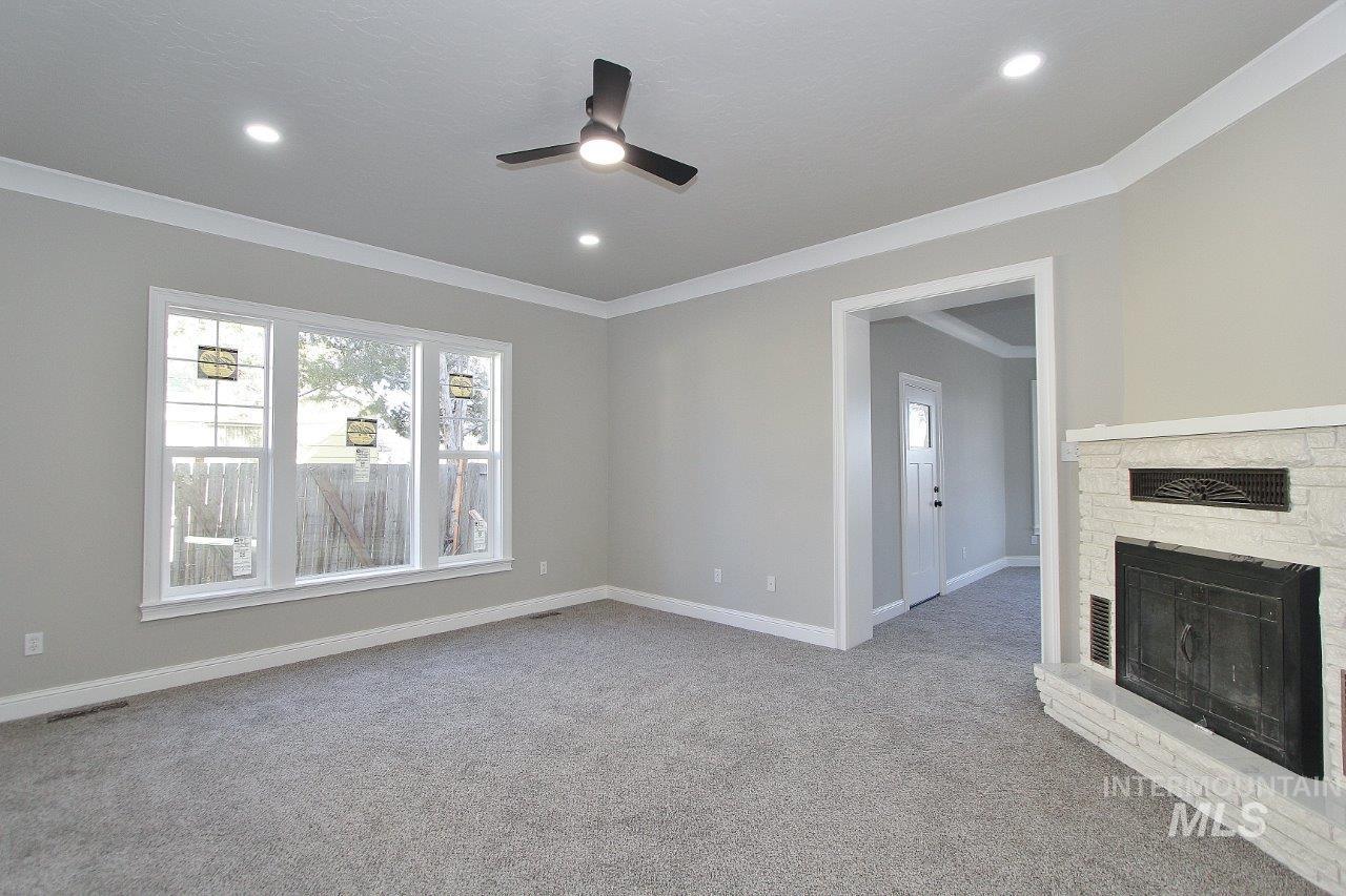121 Northwest 2nd Street Ontario, OR 97914 - Photo 11 of 32 Unfurnished living room with a stone fireplace, a ceiling fan, light carpet, and ornamental molding