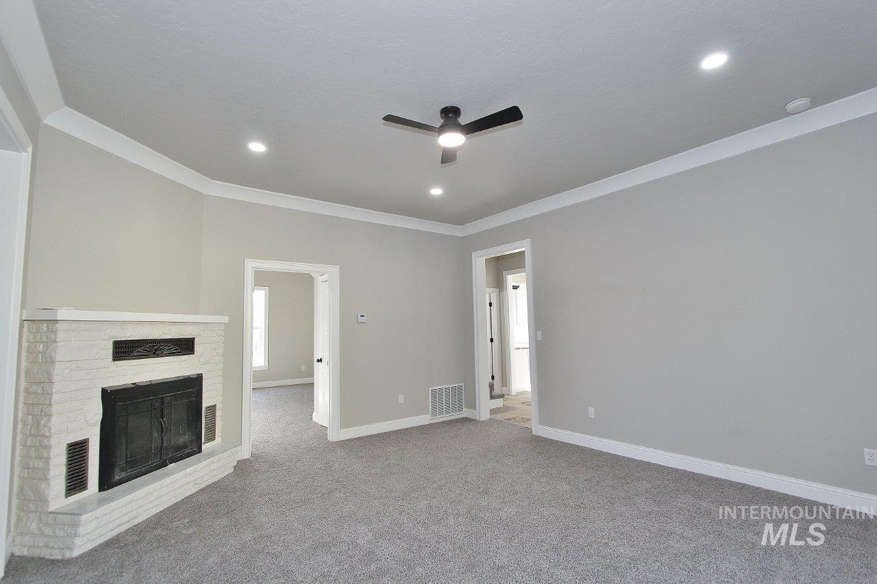 121 Northwest 2nd Street Ontario, OR 97914 - Photo 12 of 32 Unfurnished living room featuring ceiling fan, ornamental molding, a fireplace with raised hearth, carpet floors, and recessed lighting