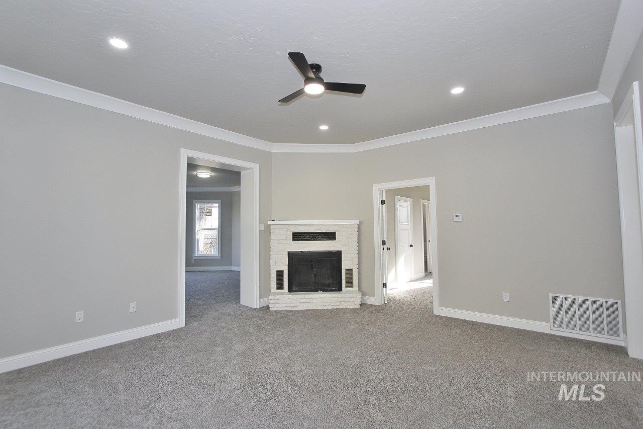 121 Northwest 2nd Street Ontario, OR 97914 - Photo 13 of 32 Unfurnished living room featuring a fireplace, crown molding, a ceiling fan, and carpet