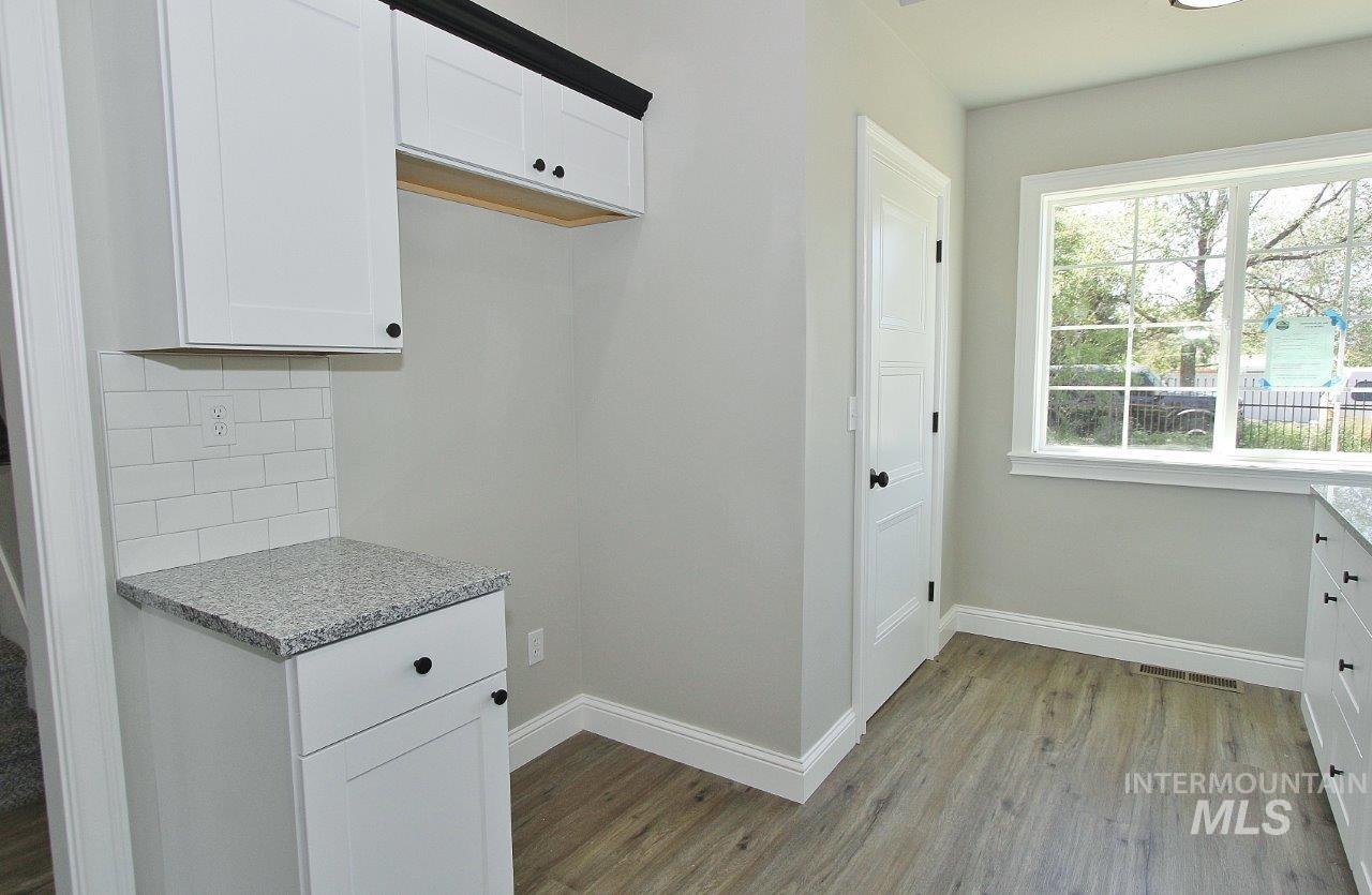 121 Northwest 2nd Street Ontario, OR 97914 - Photo 4 of 32 Kitchenette featuring white shaker cabinetry with black hardware, granite-style countertops, subway tile backsplash, and wood-finish flooring
