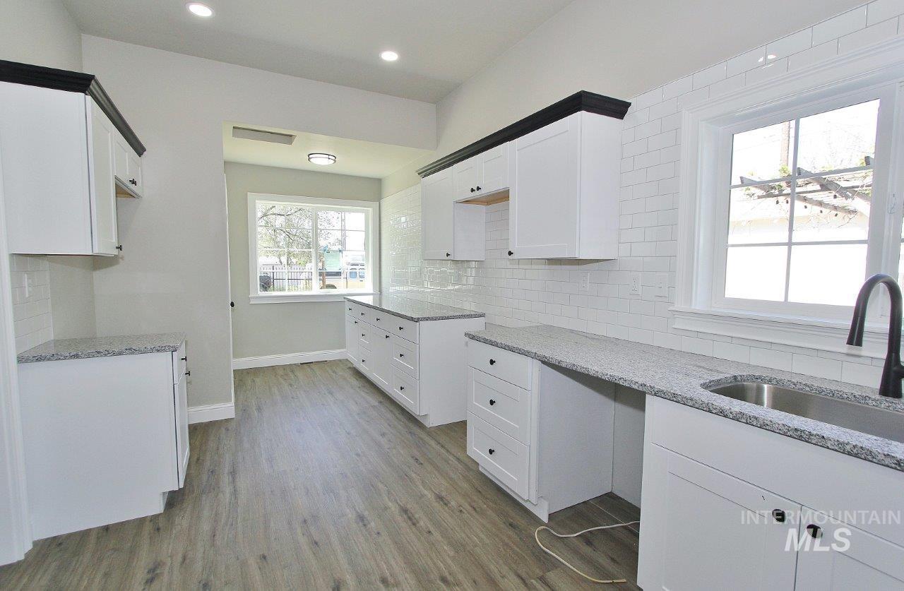 121 Northwest 2nd Street Ontario, OR 97914 - Photo 5 of 32 Bright kitchen featuring wood-finish flooring, white cabinetry with contrasting black hardware, speckled countertops, white subway tile backsplash, and a stainless steel sink with a black faucet