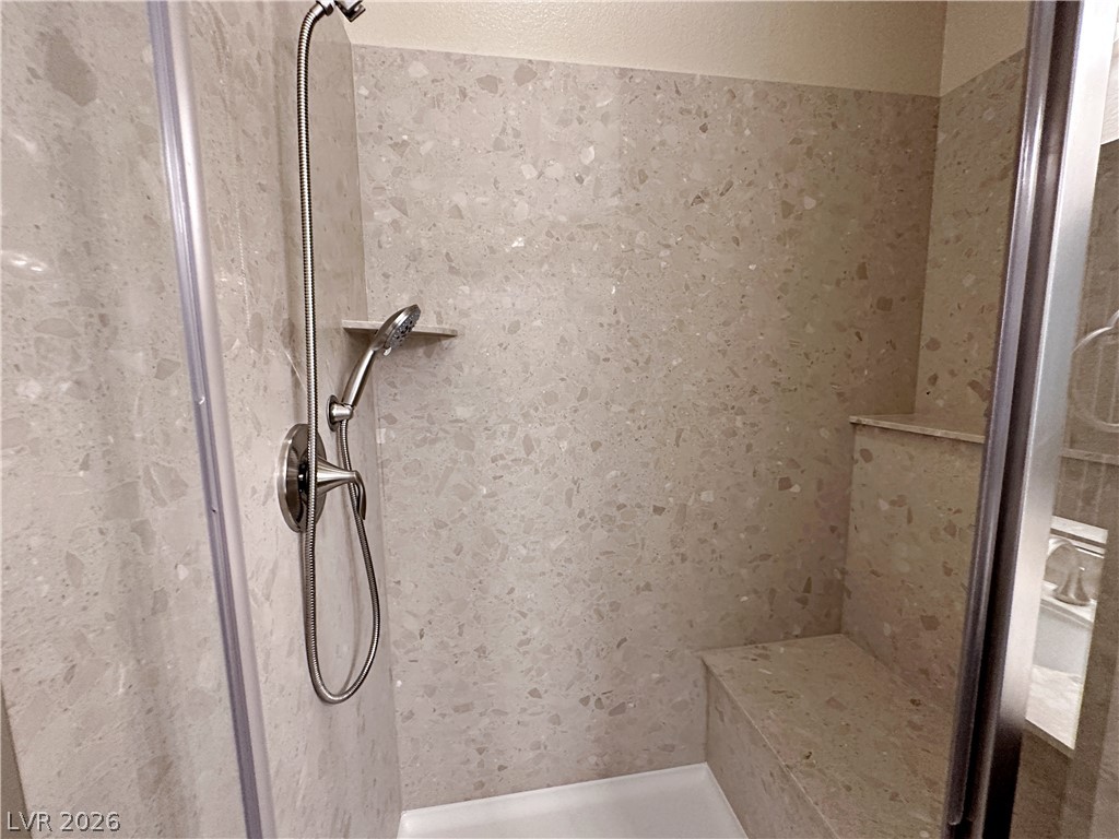 71 Newton Ridge Way Las Vegas, NV 89183 - Photo 33 of 40 A well-appointed shower space offers both a fixed and handheld showerhead, alongside a built-in bench and recessed shelving.
