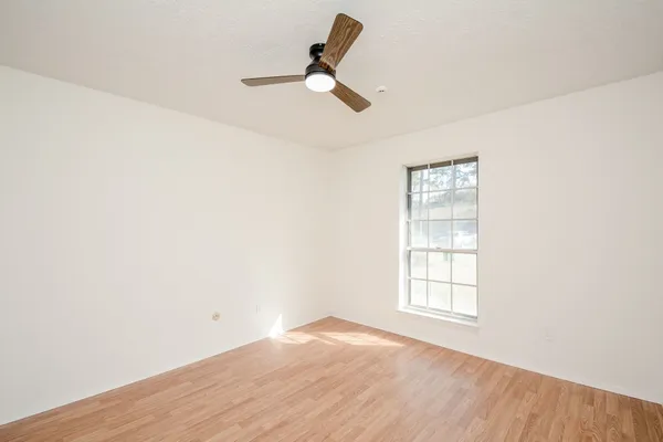 an empty room with wooden floor ceiling fan and windows