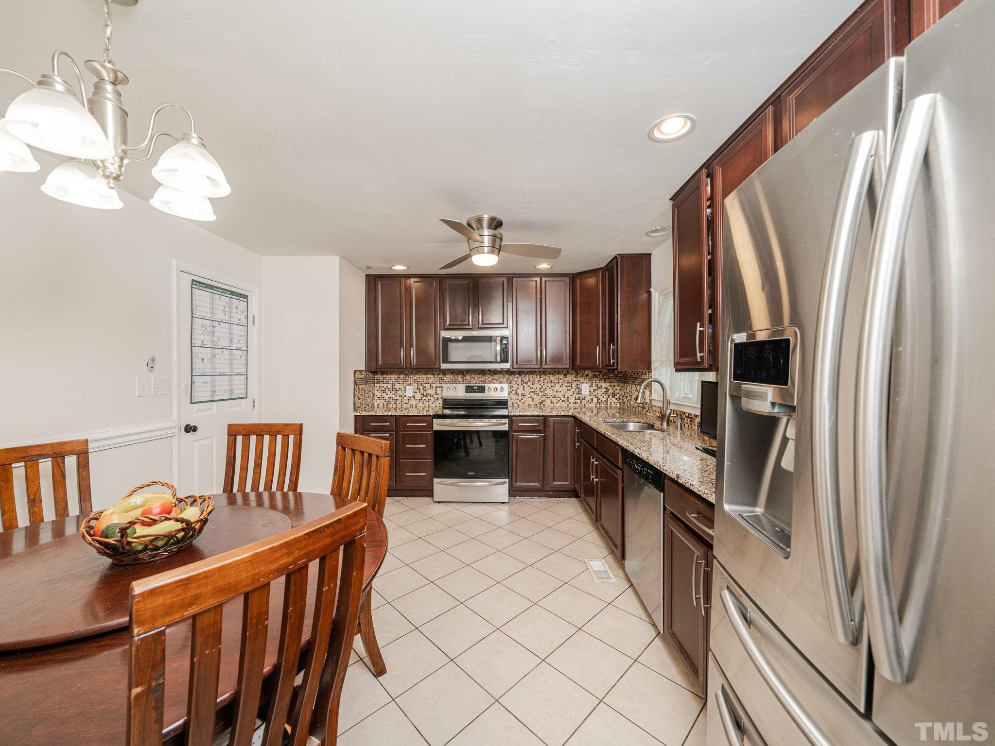 1416 Lions Way Raleigh, NC 27604 - Photo 9 of 23 a large kitchen with stainless steel appliances granite countertop a refrigerator a sink dishwasher a stove and a dining table with wooden floor