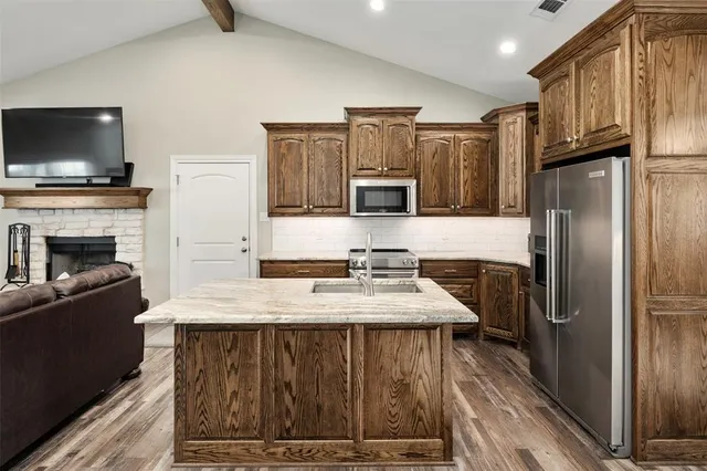 a kitchen with kitchen island granite countertop a stove top oven a refrigerator and a sink with wooden floor