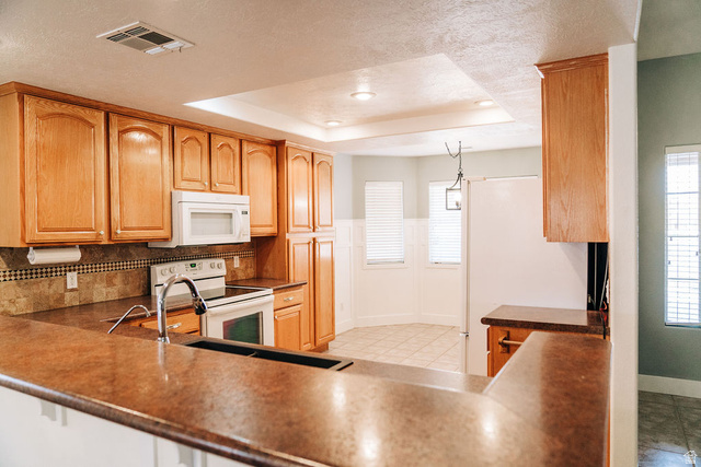 1825 West Mathis Park Place, Unit 40 St. George, UT 84770 - Photo 22 of 28 Kitchen with white appliances, a raised ceiling, dark countertops, a textured ceiling, and hanging light fixtures