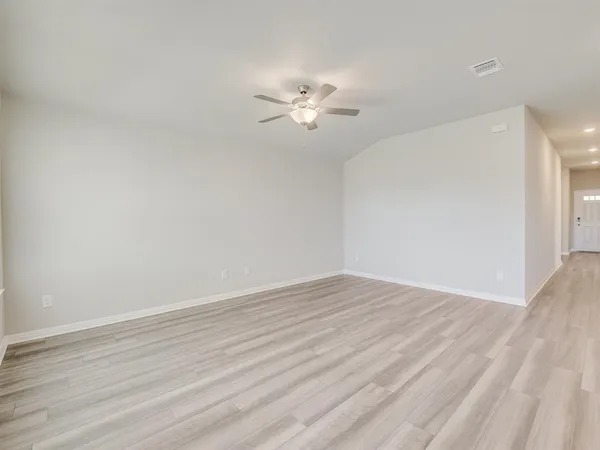a view of an empty room with wooden floor and a ceiling fan