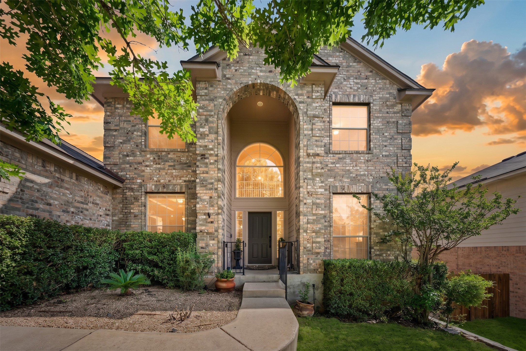 A stately brick facade, framed by lush foliage, welcomes you with an arched entryway at sunset.