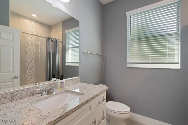 a bathroom with a granite countertop sink toilet a mirror and a window