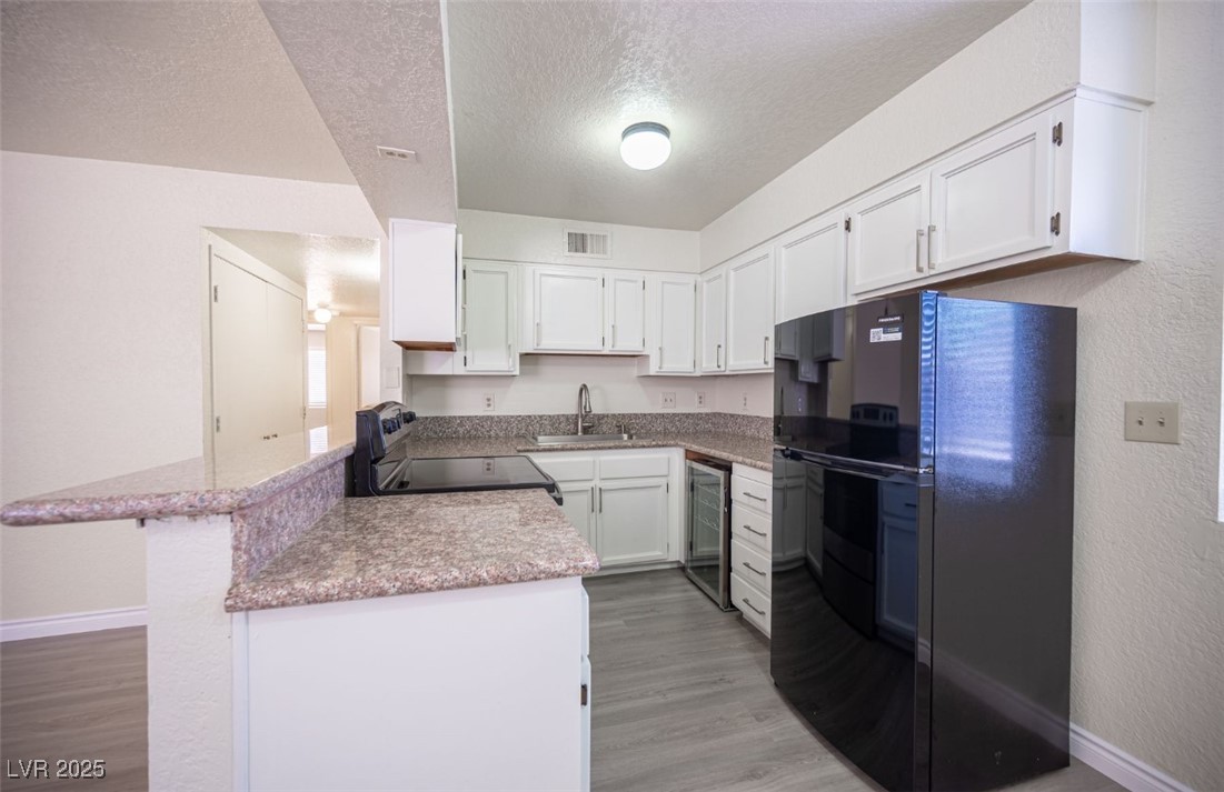 5336 Mancos Court, Unit 2 Las Vegas, NV 89119 - Photo 11 of 31 Kitchen with black appliances, white cabinets, a peninsula, beverage cooler, and a textured ceiling