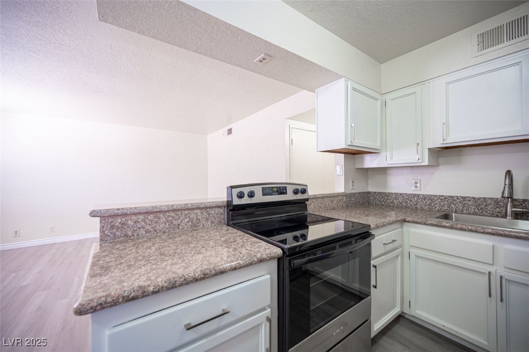5336 Mancos Court, Unit 2 Las Vegas, NV 89119 - Photo 13 of 31 Kitchen featuring stainless steel electric stove, white cabinetry, light wood-style floors, and a textured ceiling