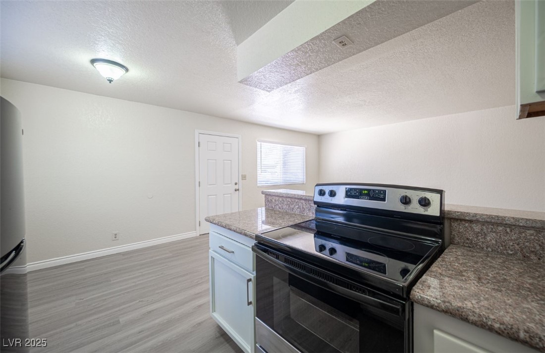 5336 Mancos Court, Unit 2 Las Vegas, NV 89119 - Photo 15 of 31 Kitchen with range with electric stovetop, a textured ceiling, freestanding refrigerator, light wood finished floors, and white cabinetry